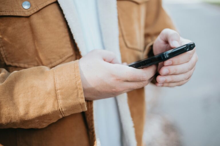 Person in a brown jacket typing on a phone