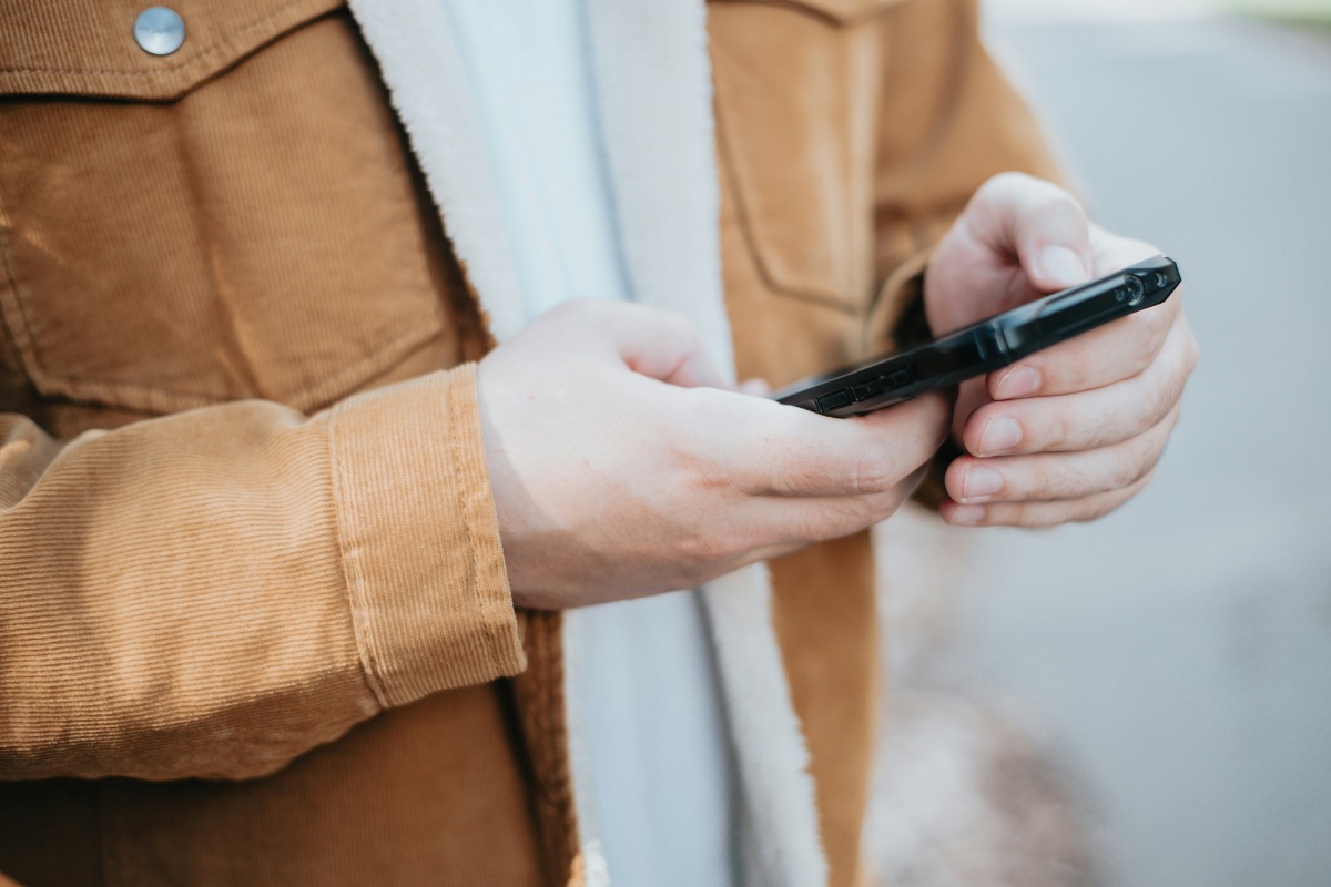 Person in a brown jacket typing on a phone